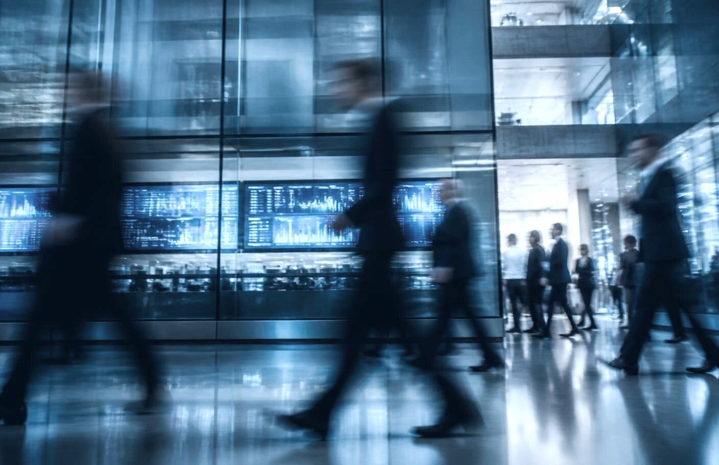 Motion-blurred business people moving fast through a glass lobby past live market data screens